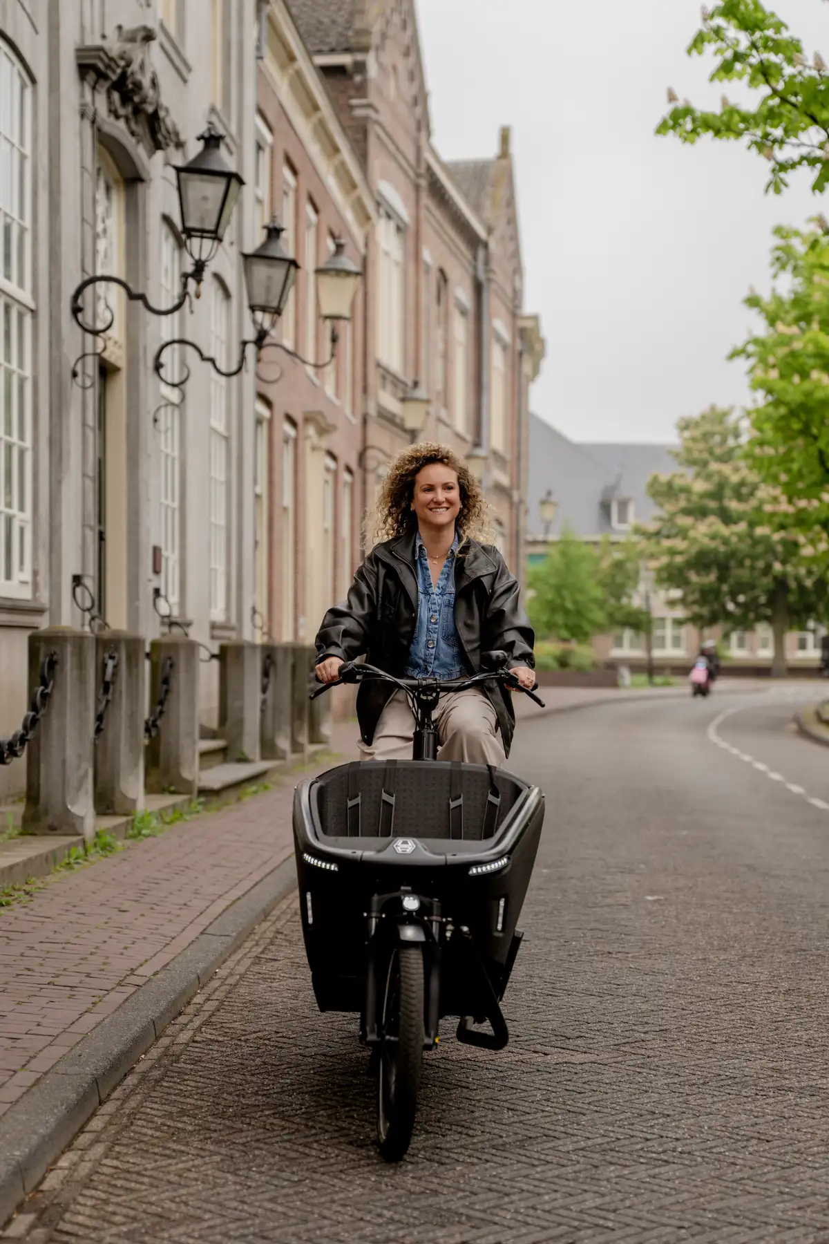 Vrouw fietst op een zwarte elektrische bakfiets door een stadsstraat.